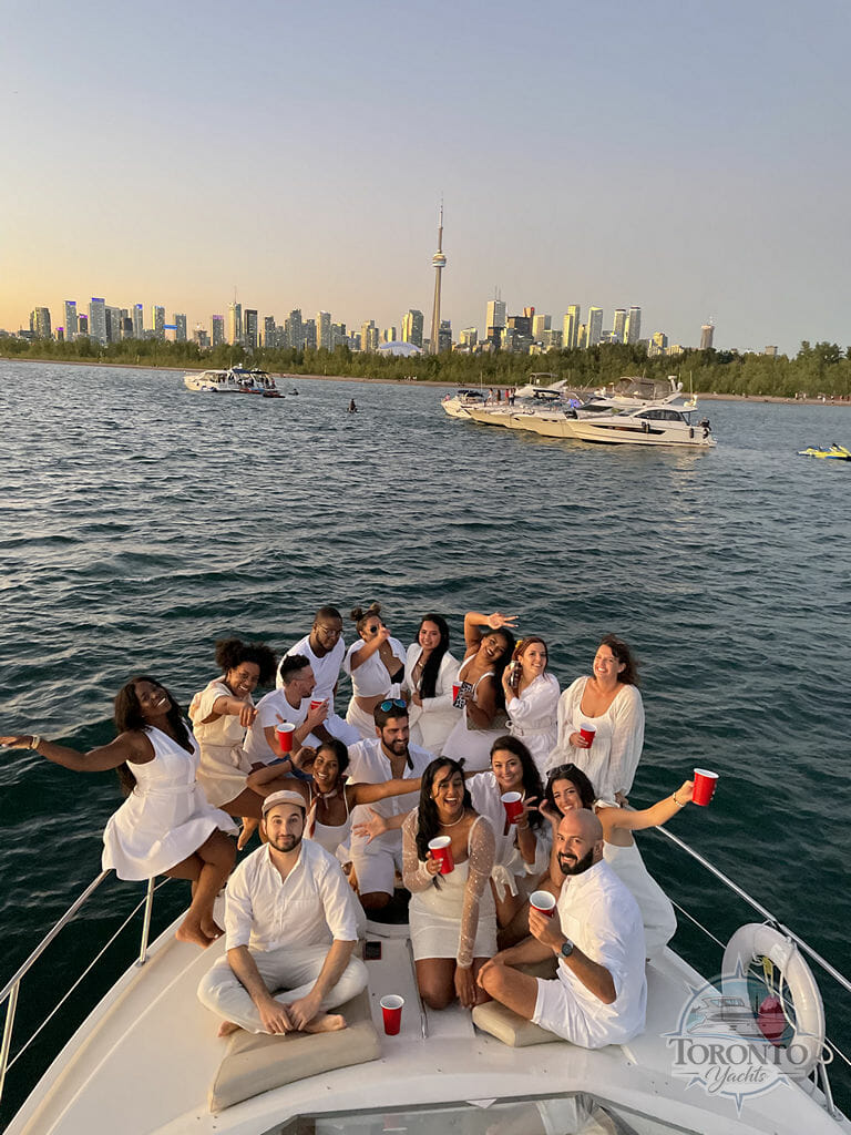 Toronto Yachts presents a gathering of people enjoying a party on a sailboat, with the Toronto city and other rental boats in the backdrop.
